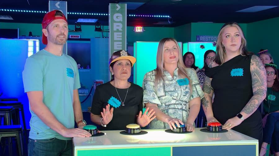 Four players standing at the buzzers with their name tags on