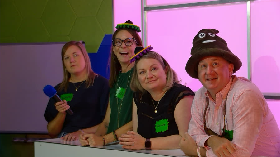 Four guests in party hats at the podium, one holding the blue microphone