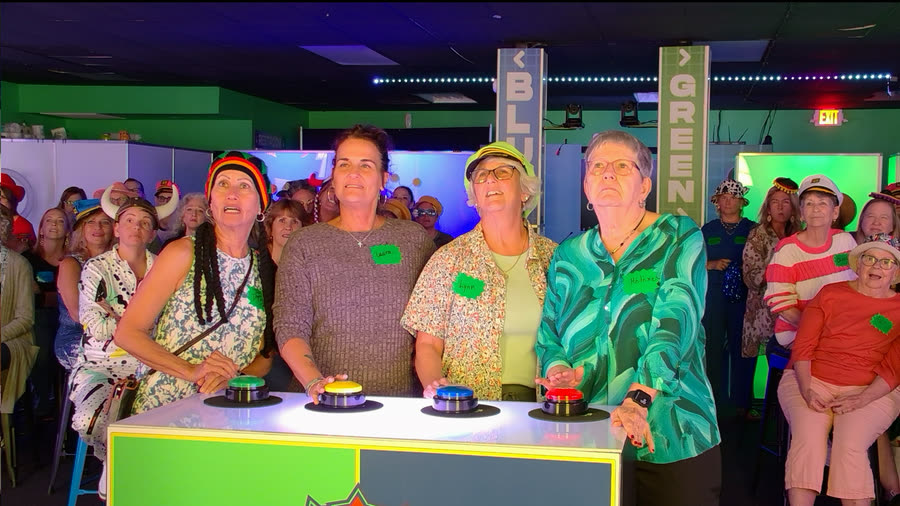 Four players at the buzzers in novelty hats, a full room watching