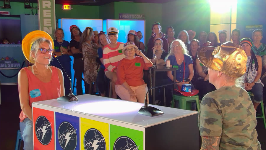The host facing a player across the podium while the audience watches
