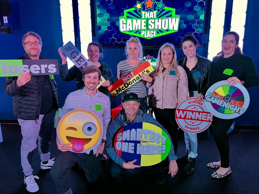 A group posing with novelty signs and props under the studio's logo screen